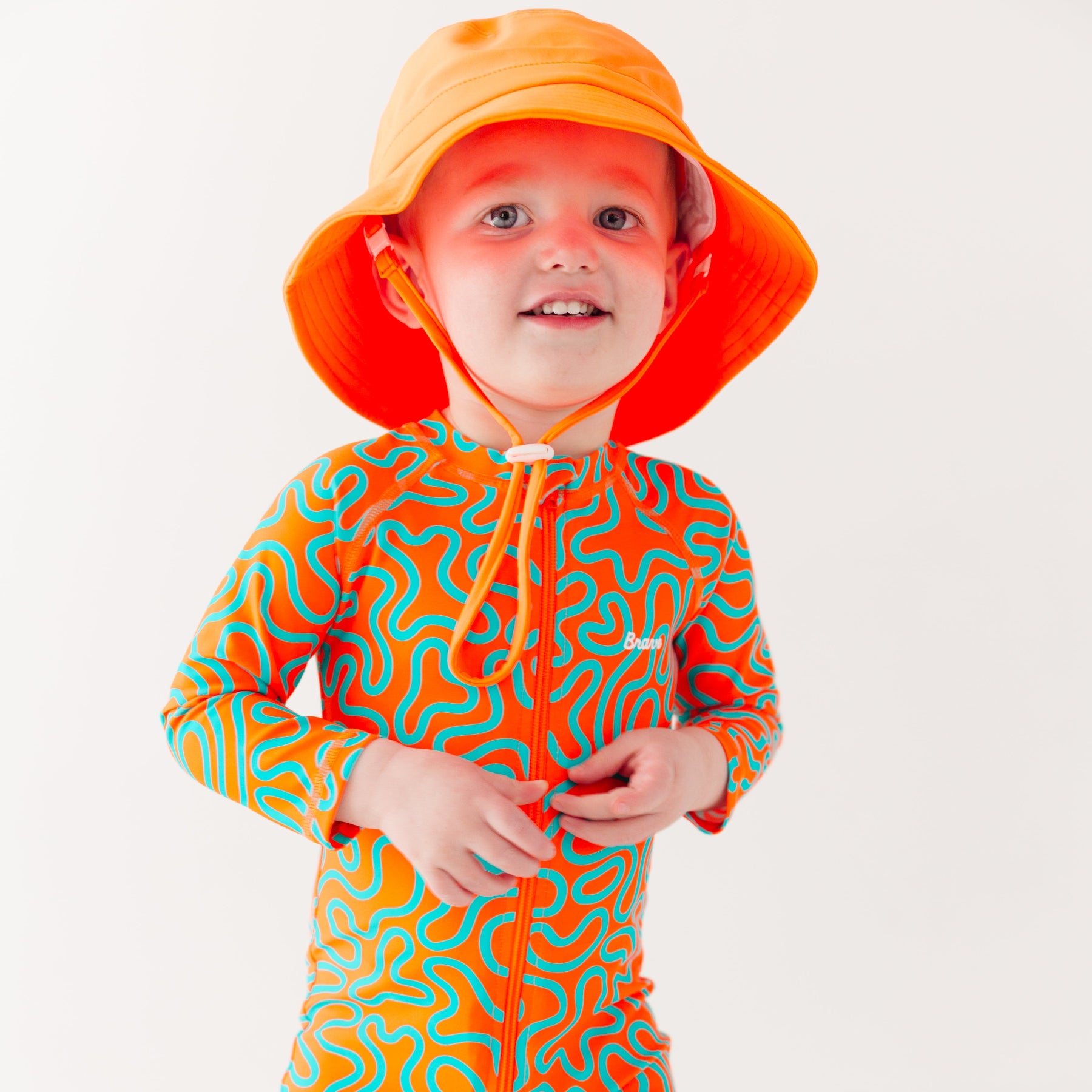Child wearing a colorful swimsuit with a squiggly pattern and an orange bucket hat on a white background