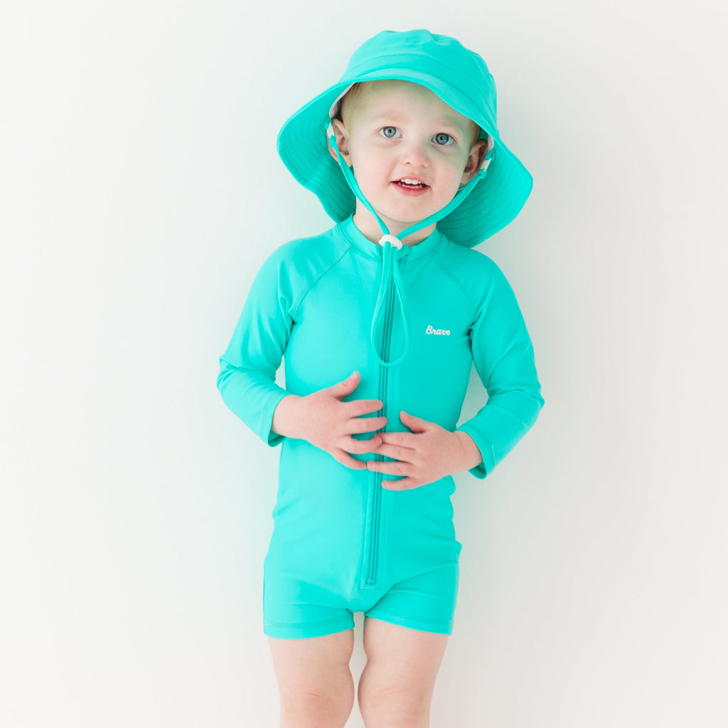Child wearing a turquoise boy swimsuit and matching bucket hat on a white background