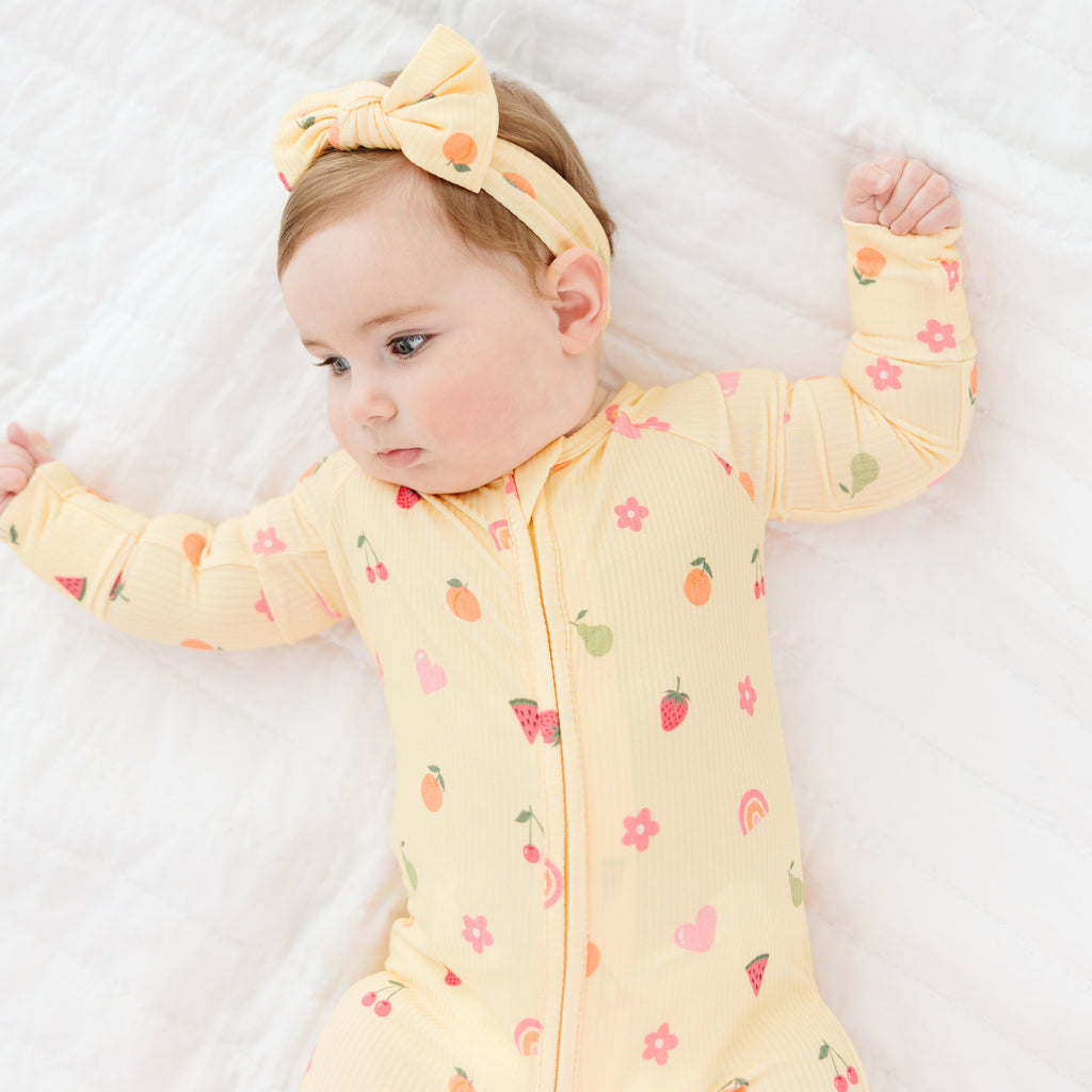 Baby wearing a yellow outfit with fruits patterns and a matching headband on a white background