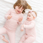 Two children in matching pink striped pajamas lying on a white surface.