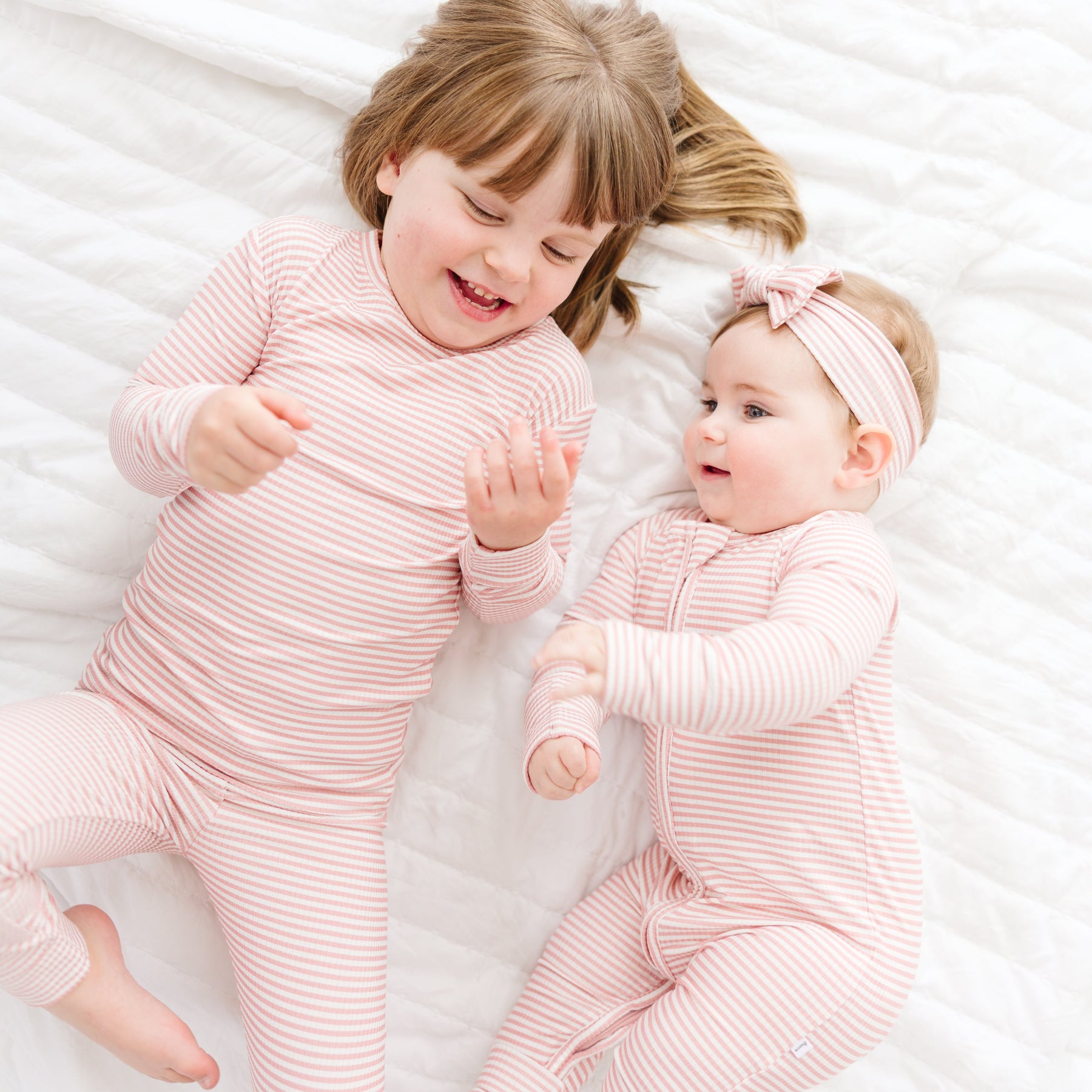 Two children in matching pink striped pajamas lying on a white surface.