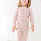 Child wearing a pink striped long sleeve pajama set on a white background