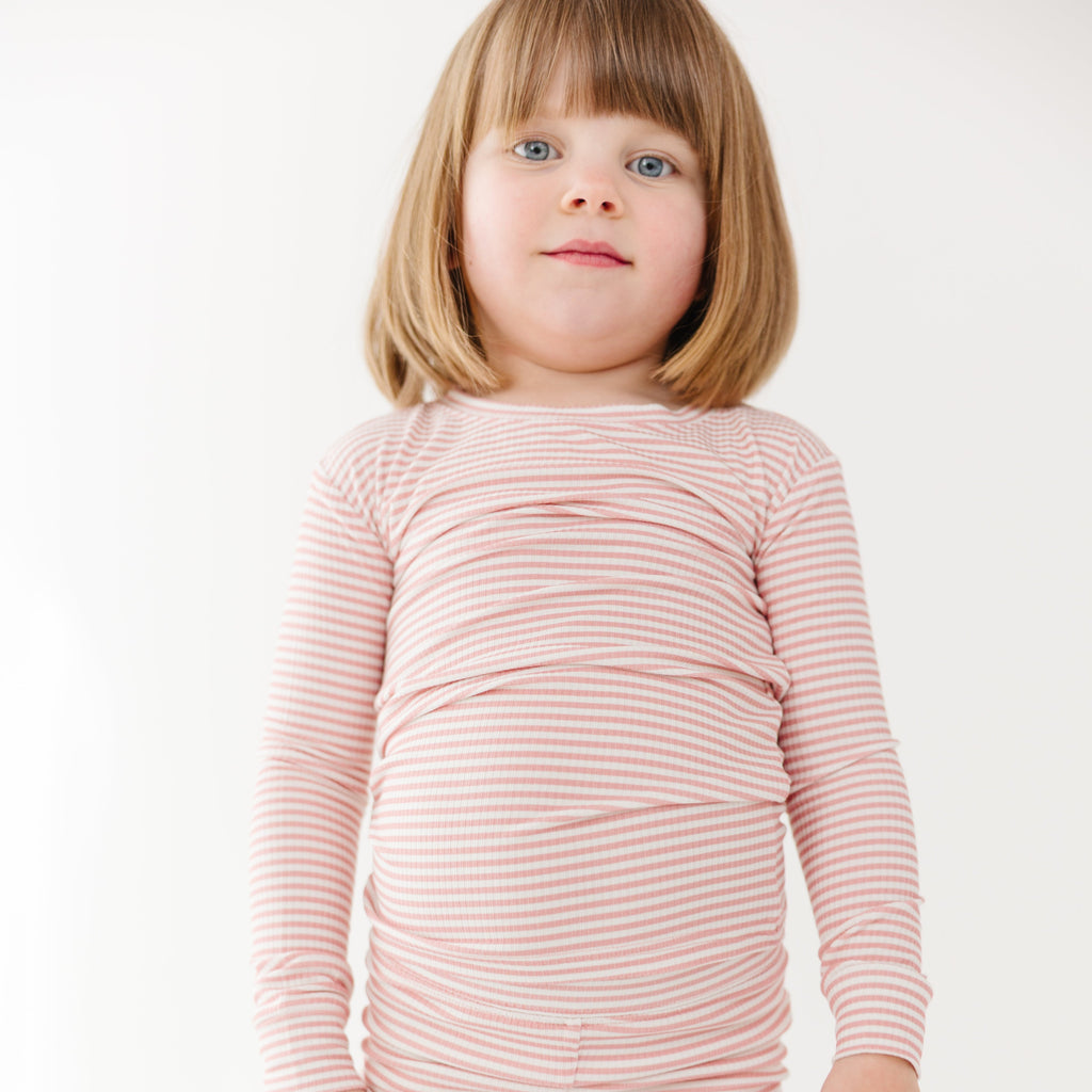 Child wearing a pink striped long sleeve pajama on a white background