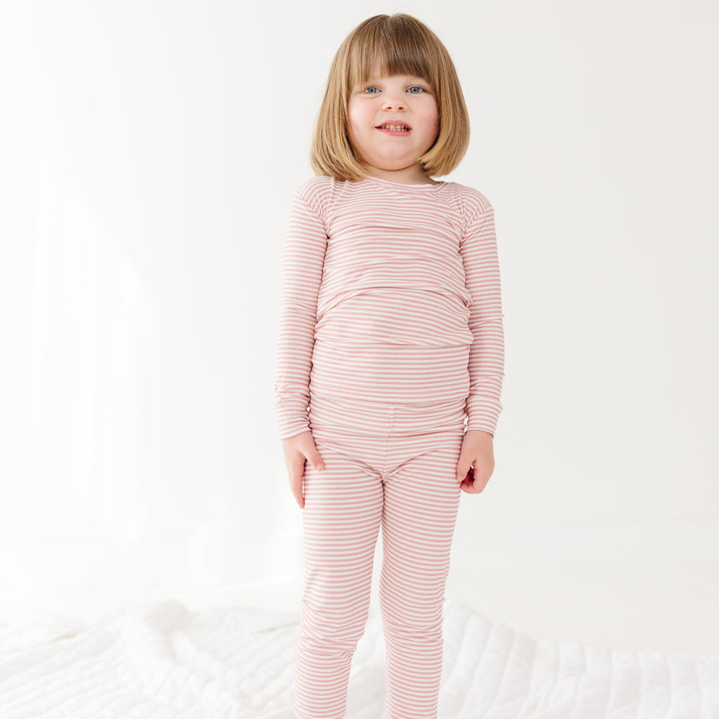 Child wearing a pink striped long sleeve pajama set on a white background