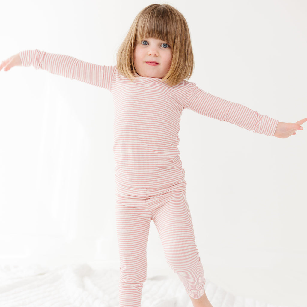 Child wearing a pink striped long sleeve pajama set on a white background