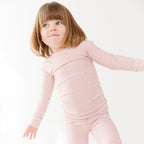 Child wearing a pink striped long sleeve pajama set on a white background