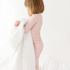 Child in a pink striped long sleeve pajama set holding a white blanket on a white background