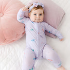 Baby in a purple onesie with animal prints lying on a pink cushion.