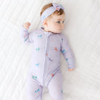 Baby wearing a light purple onesie with colorful patterns on a white textured surface