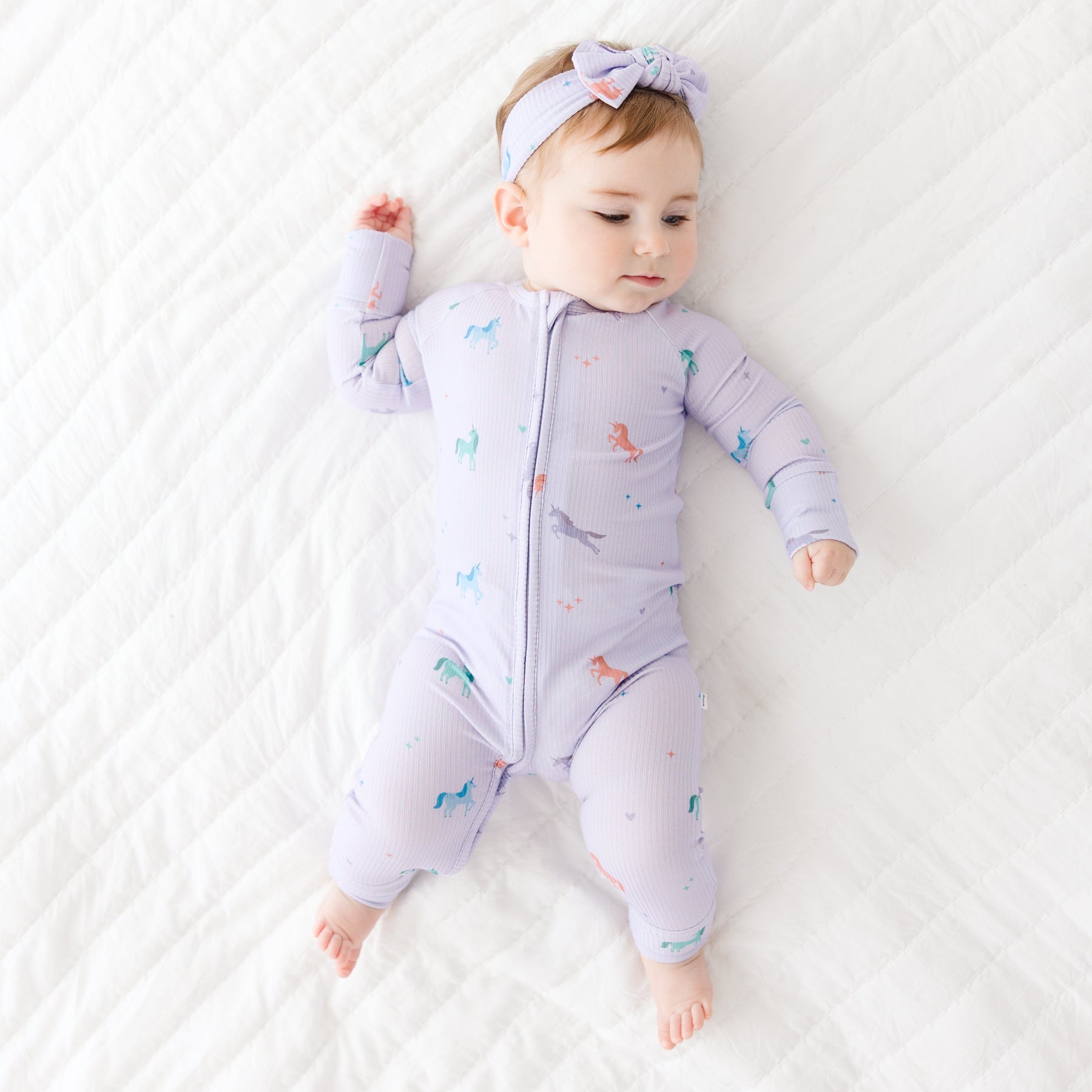 Baby wearing a purple onesie with animal prints on a white blanket
