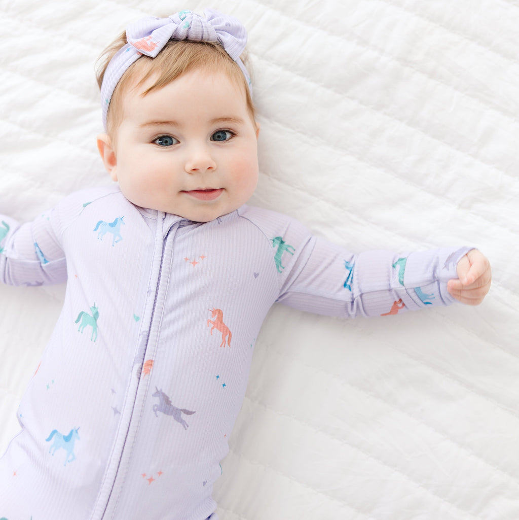 Baby wearing a purple onesie with animal prints on a white blanket