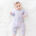 Baby wearing a purple Zip Romper with colorful unicorn designs on a white textured surface