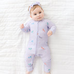 Baby wearing a purple Zip Romper with colorful unicorn designs on a white textured surface