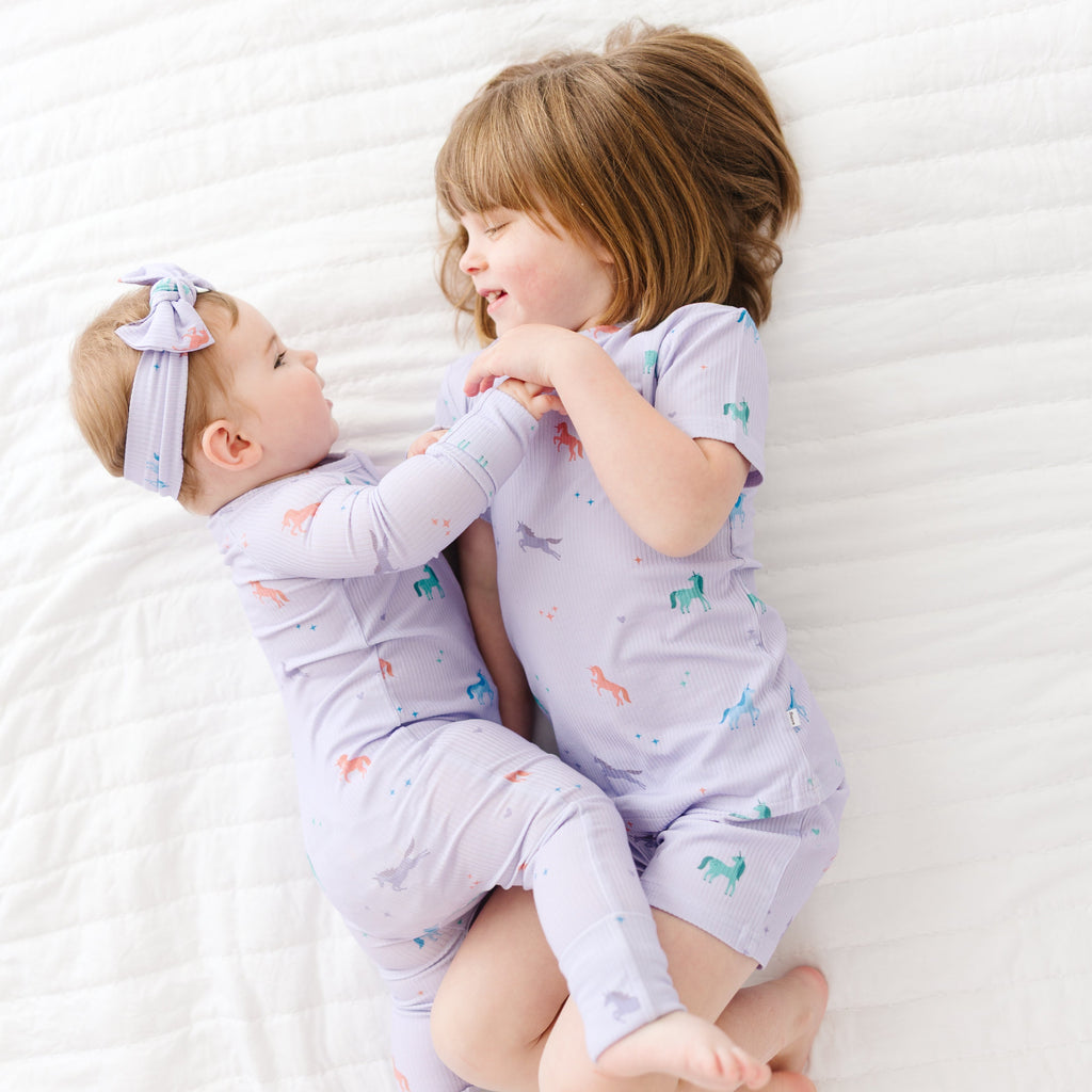 Two children in matching pajamas lying on a white bed.