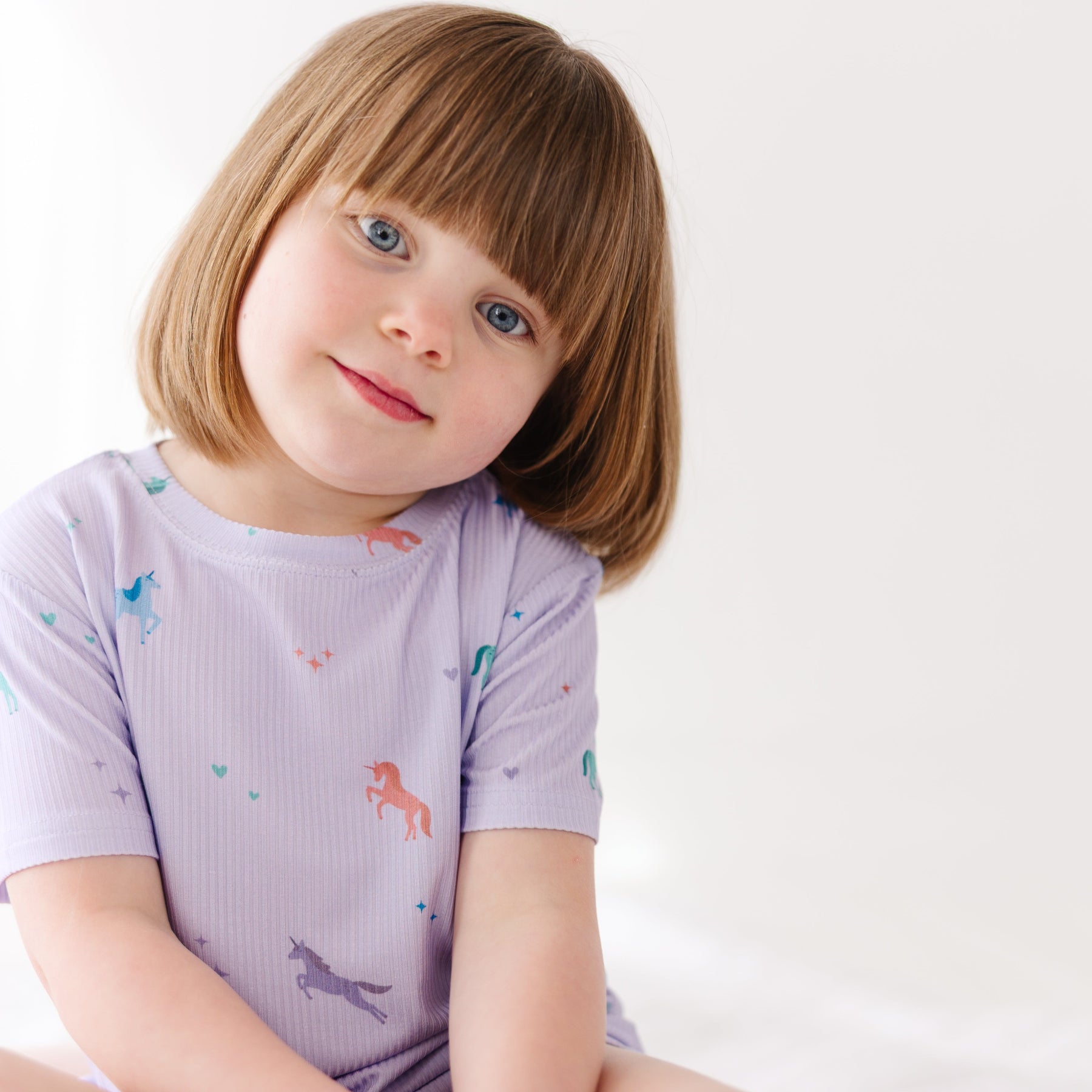 Young girl wearing a light purple pajama set with animal prints on a white background