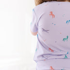 Child wearing a light purple pajama set with colorful horse patterns on a white background