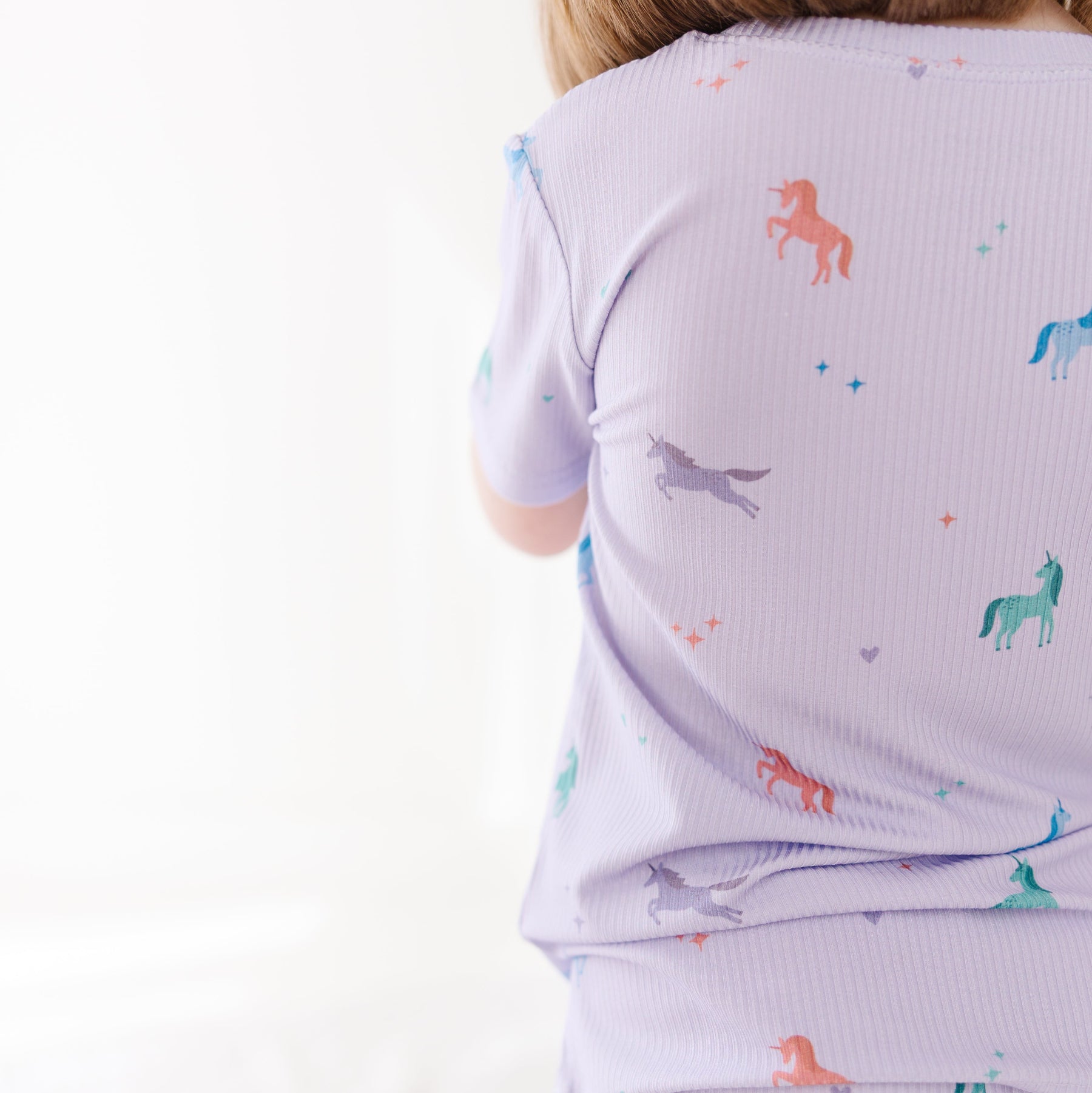 Child wearing a light purple pajama set with colorful horse patterns on a white background