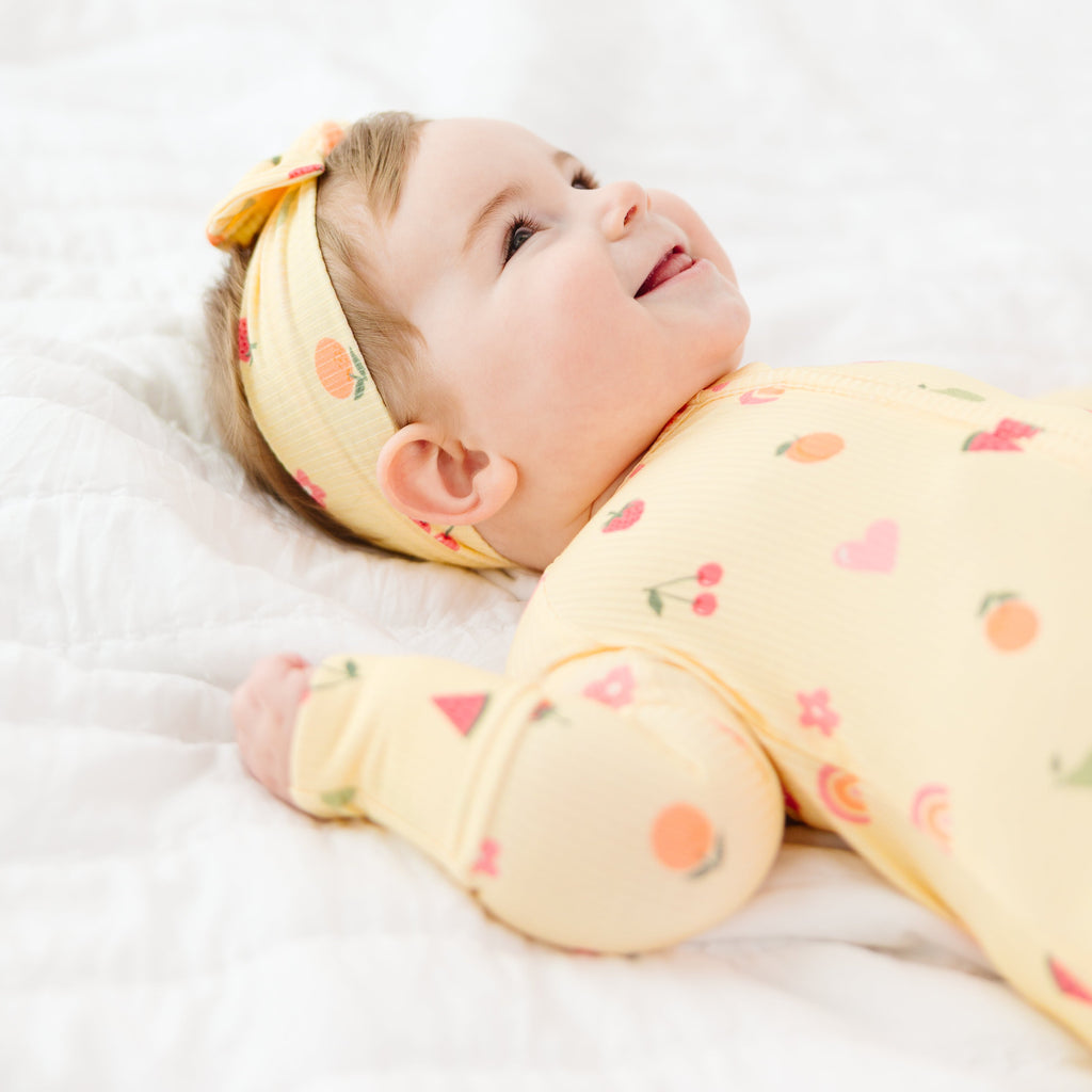 Baby wearing a yellow outfit with fruits patterns and a matching headband on a white background