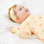 Baby wearing a yellow outfit with fruits patterns and a matching headband on a white background