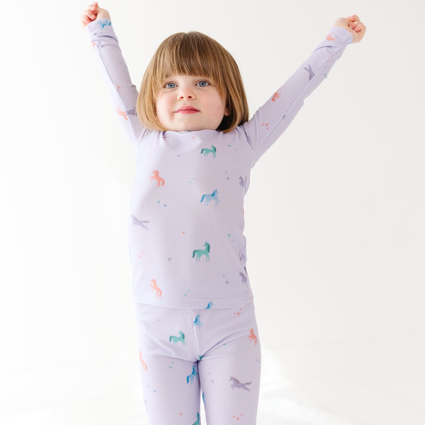 Child wearing a purple pajama set with unicorn prints on a white background