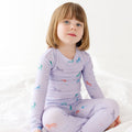 Child wearing a purple pajama set with unicorn prints on a white background