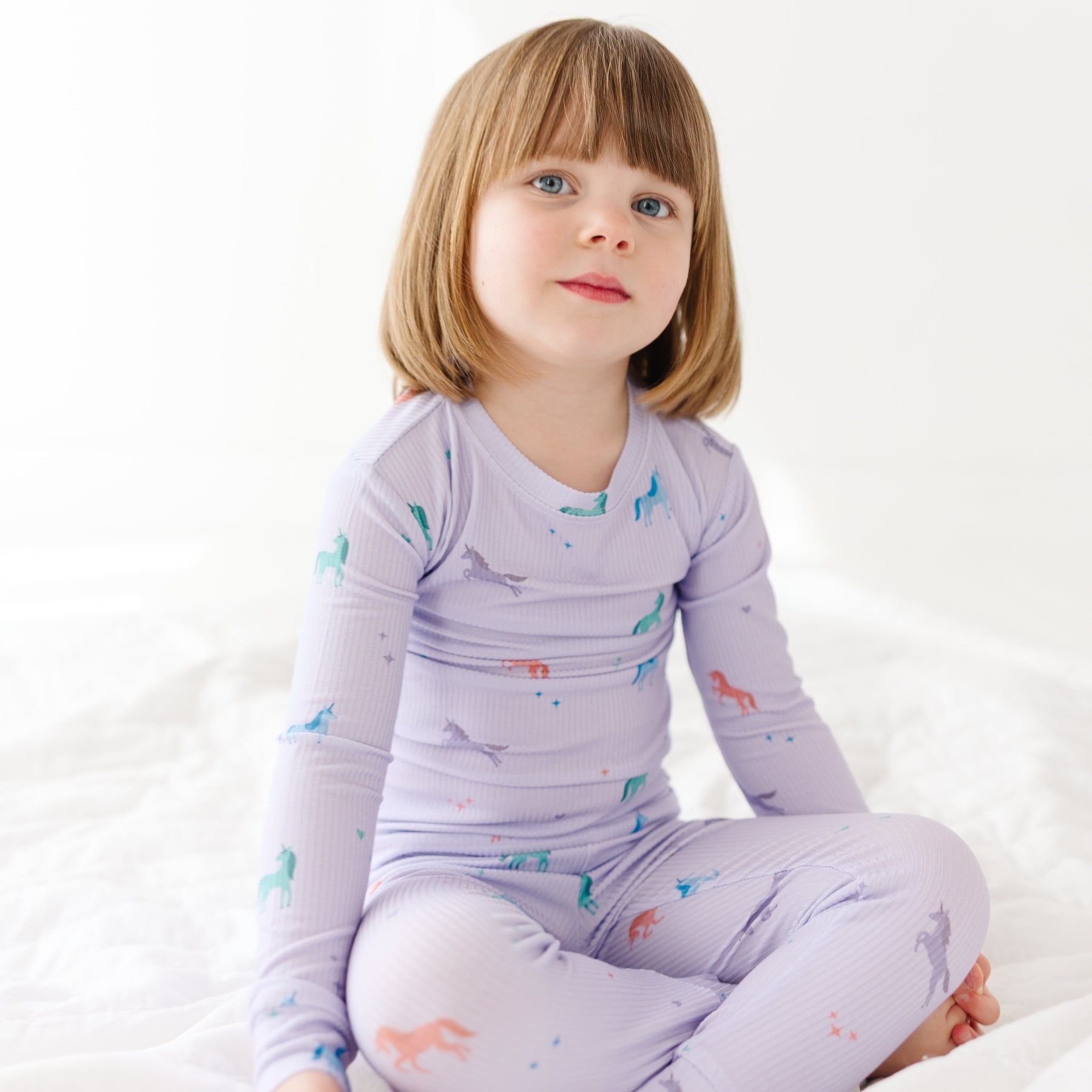 Child wearing a purple pajama set with unicorn prints on a white background