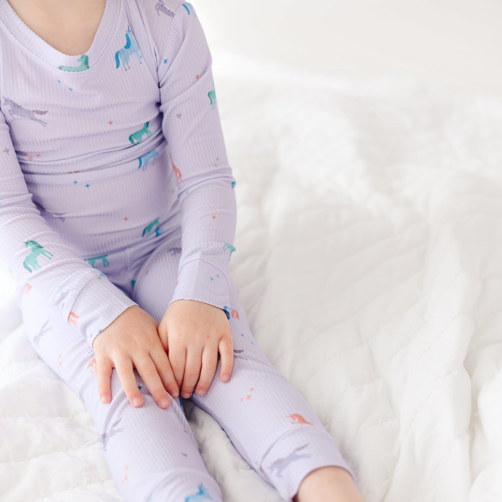 Child wearing a purple pajama set with unicorn prints on a white background
