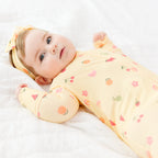 Baby wearing a yellow outfit with fruits patterns and a matching headband on a white background