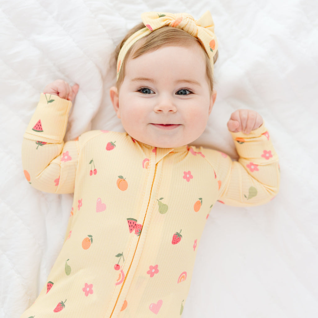 Baby wearing a yellow onesie with fruit patterns on a white background