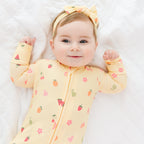 Baby wearing a yellow onesie with fruit patterns on a white background