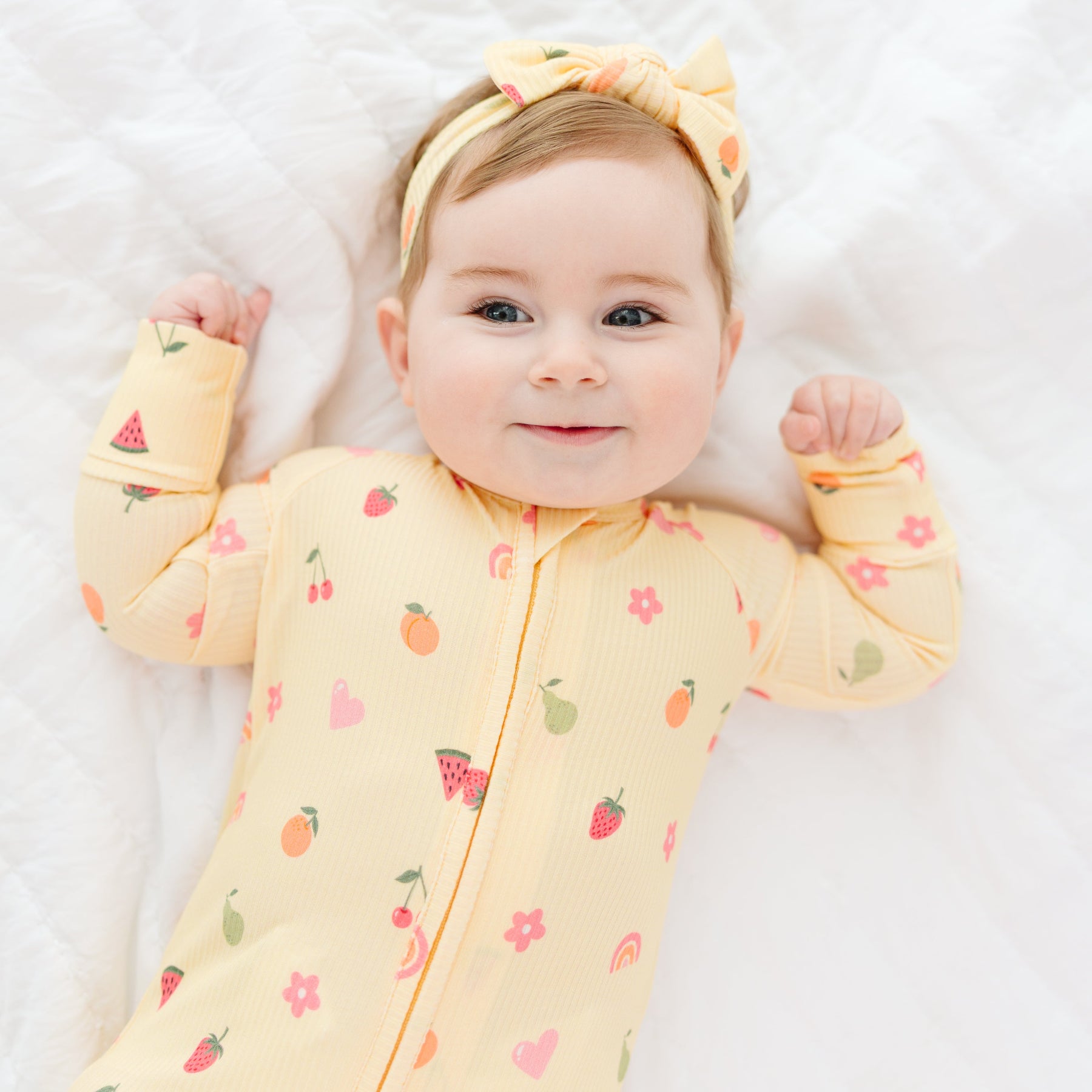 Baby wearing a yellow onesie with fruit patterns on a white background