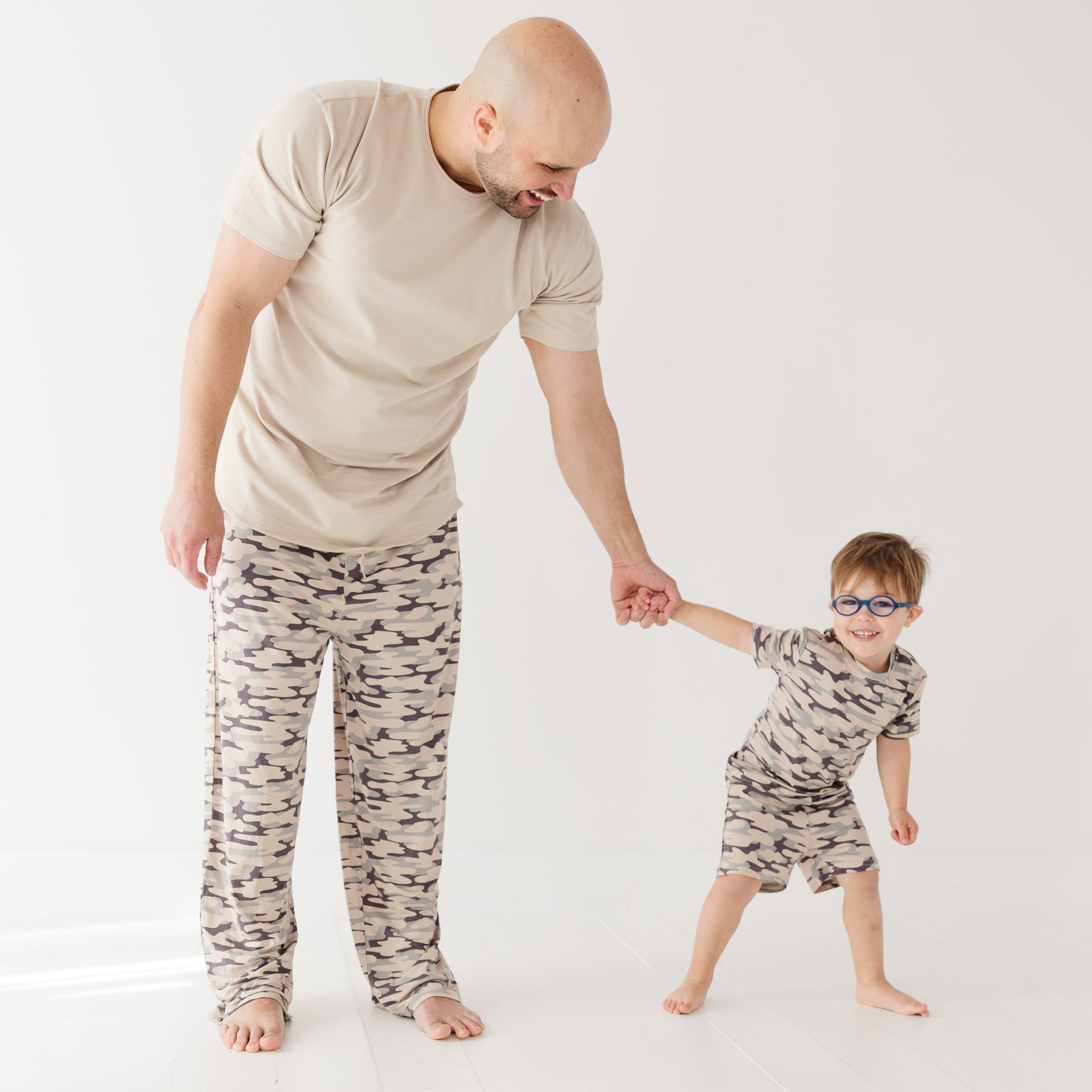 Man and child wearing matching camouflage pajamas on a white background