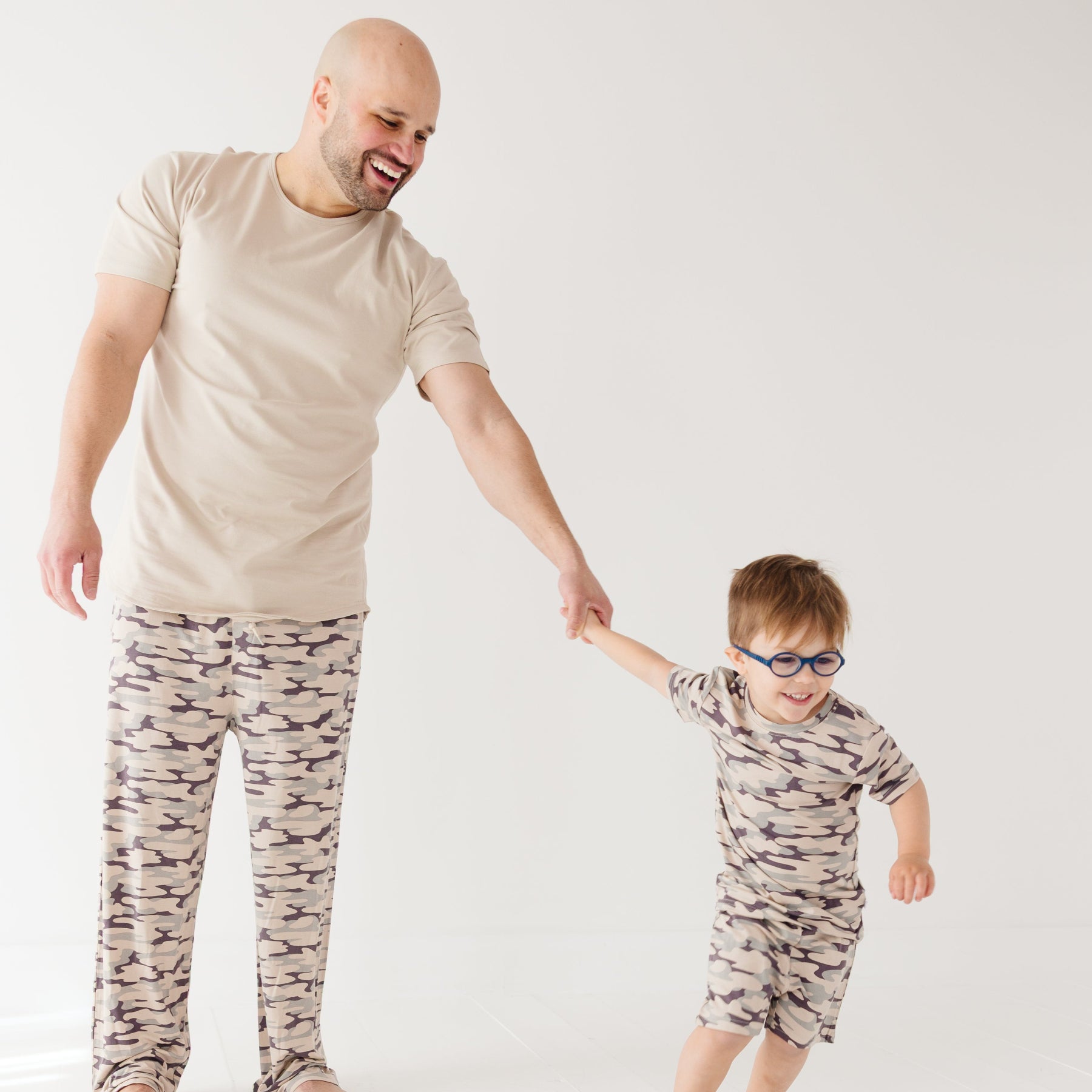Man and child wearing matching camouflage outfits on a white background
