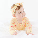 Baby wearing a yellow outfit with fruits patterns and a matching headband on a white background