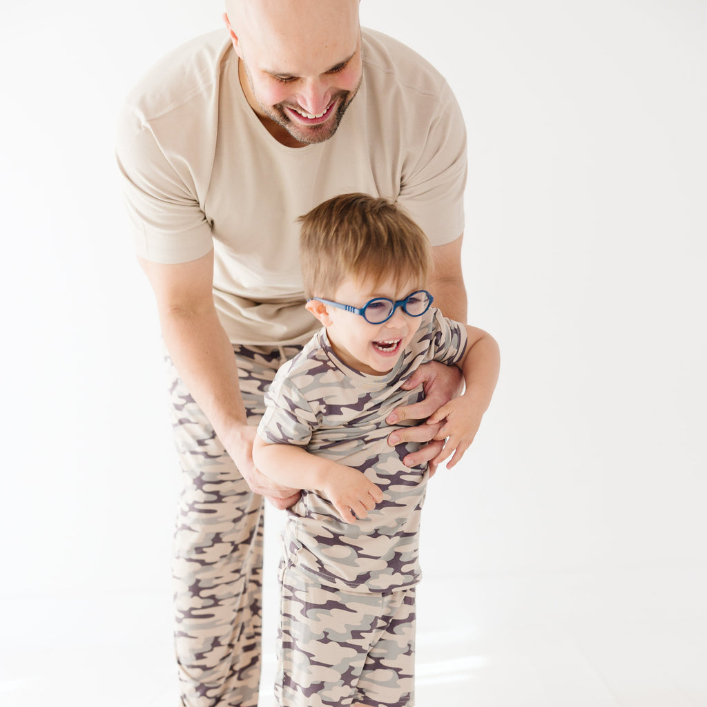 Man and child wearing matching camouflage outfits on a white background