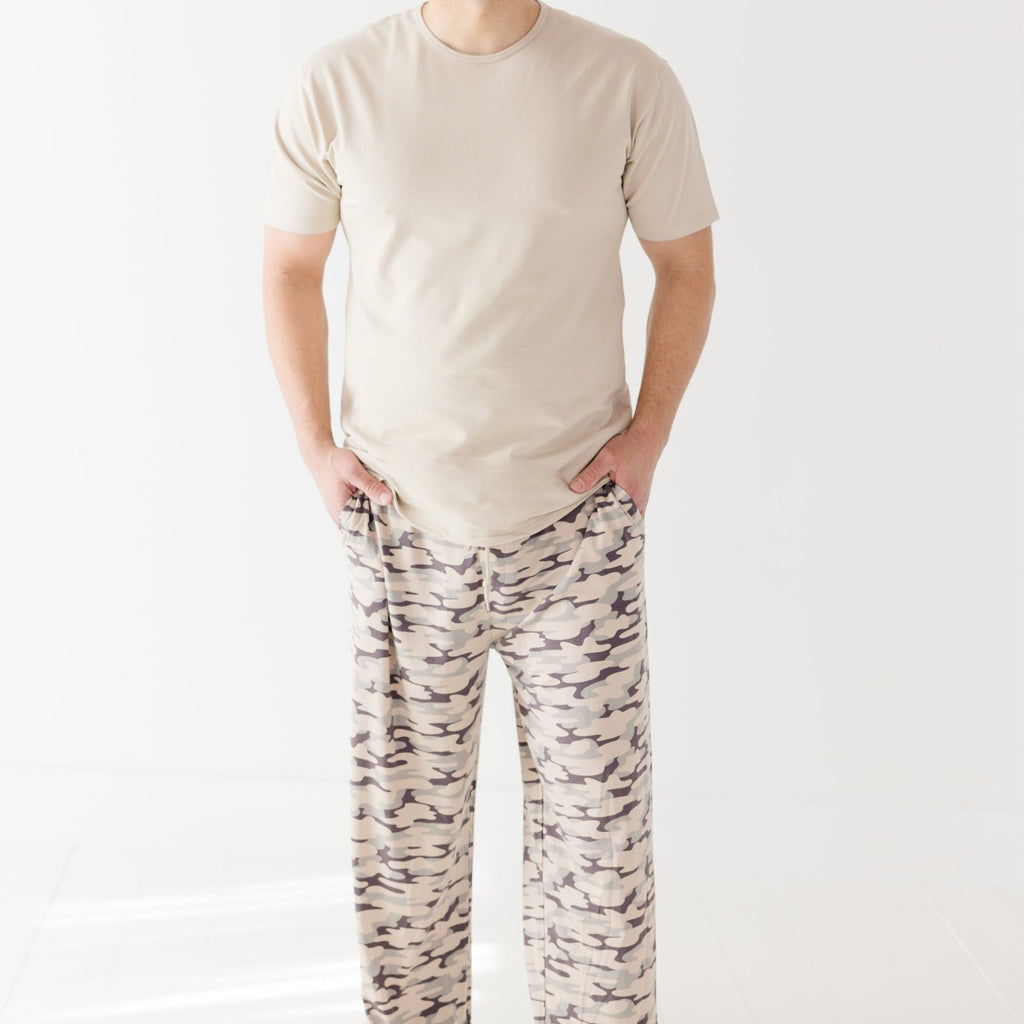 Man wearing a beige t-shirt and camouflage-patterned pants on a white background