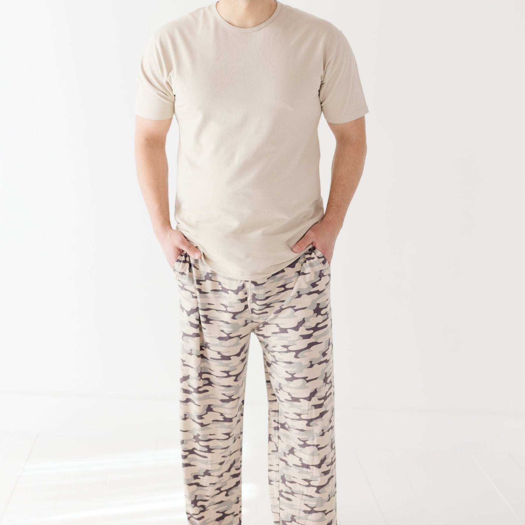 Man wearing a beige t-shirt and camouflage-patterned pants on a white background