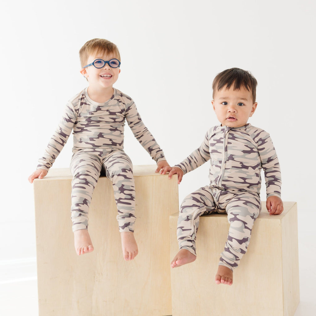 Two children wearing matching camouflage pajamas sitting on a white background