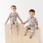 Two children wearing matching camouflage pajamas sitting on a white background