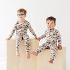 Two children wearing matching camouflage pajamas sitting on a white background