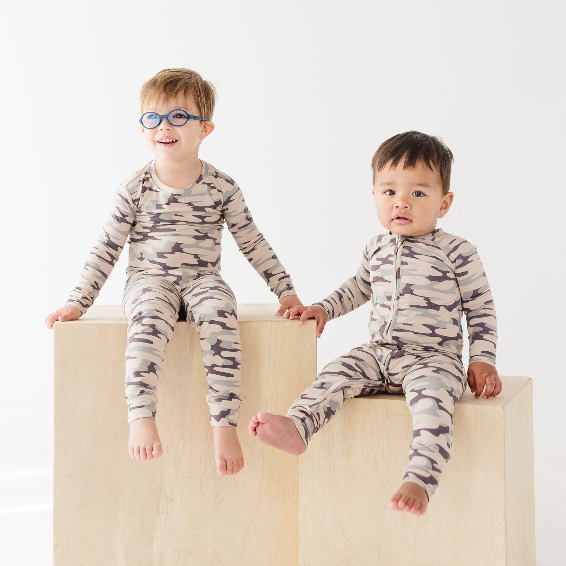 Two children wearing matching camouflage pajamas sitting on a white background
