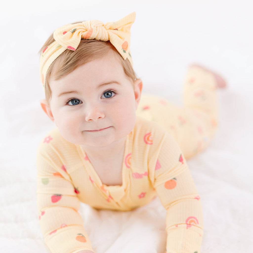Baby wearing a yellow outfit with fruits patterns and a matching headband on a white background