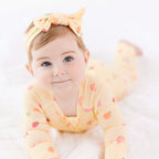 Baby wearing a yellow outfit with fruits patterns and a matching headband on a white background