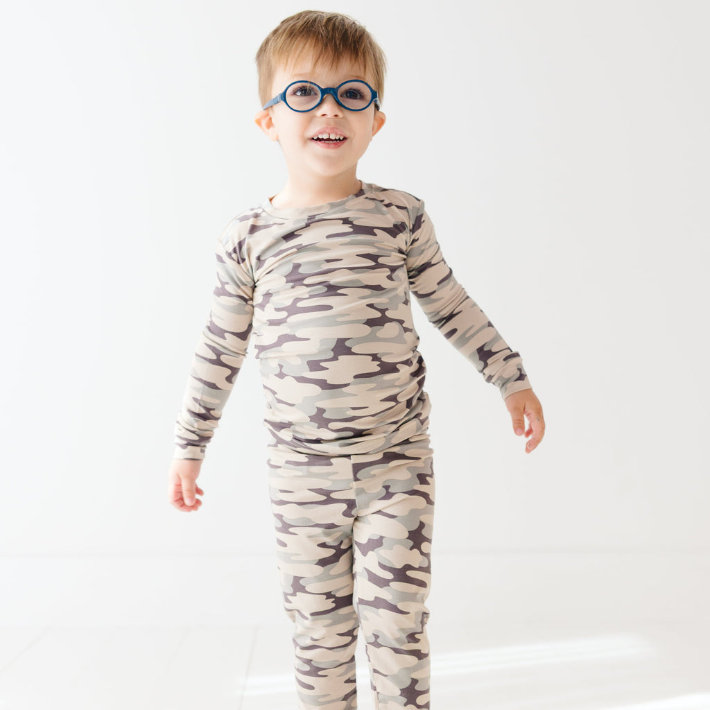 Child wearing a camouflage long sleeve pajama set on a white background