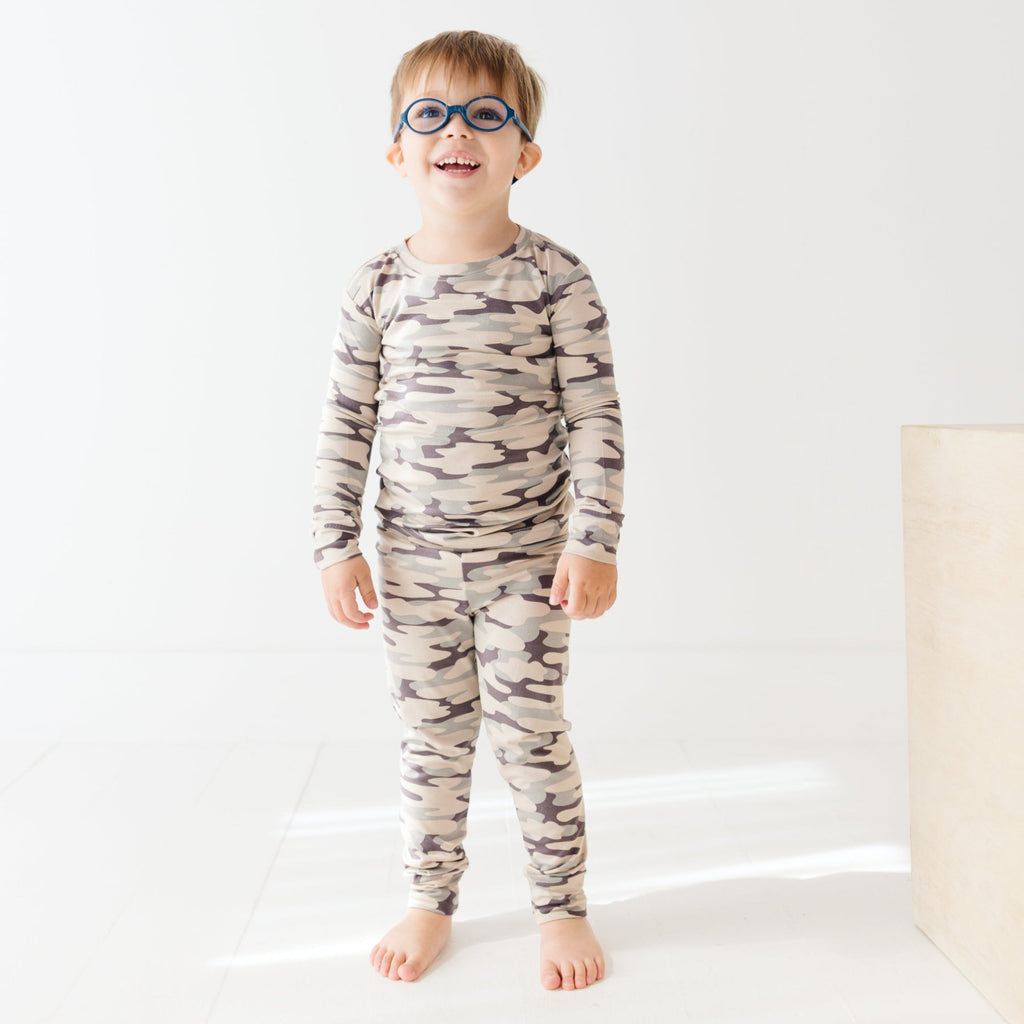 Child wearing a camouflage long sleeve pajama set on a white background