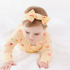 Baby wearing a yellow outfit with fruits patterns and a matching headband on a white background