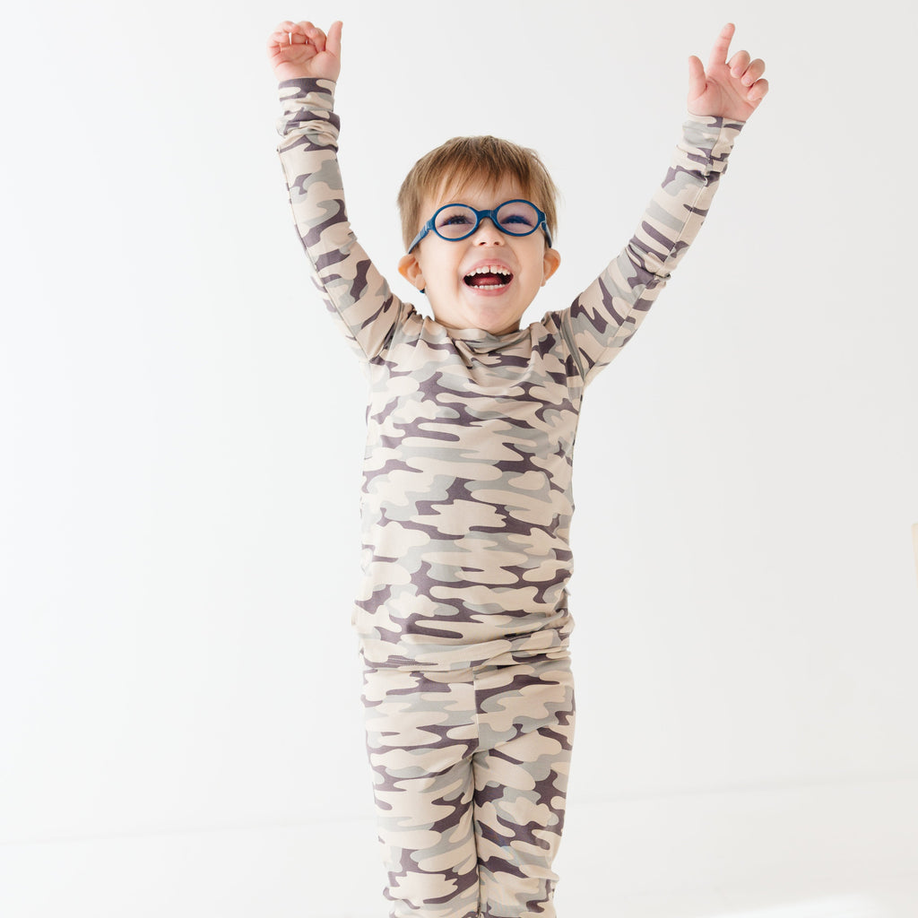 Child wearing a camouflage long sleeve pajama set on a white background