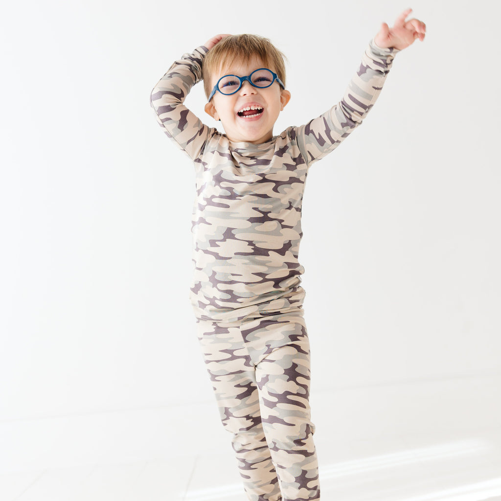 Child wearing a camouflage long sleeve pajama set on a white background