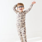 Child wearing a camouflage long sleeve pajama set on a white background