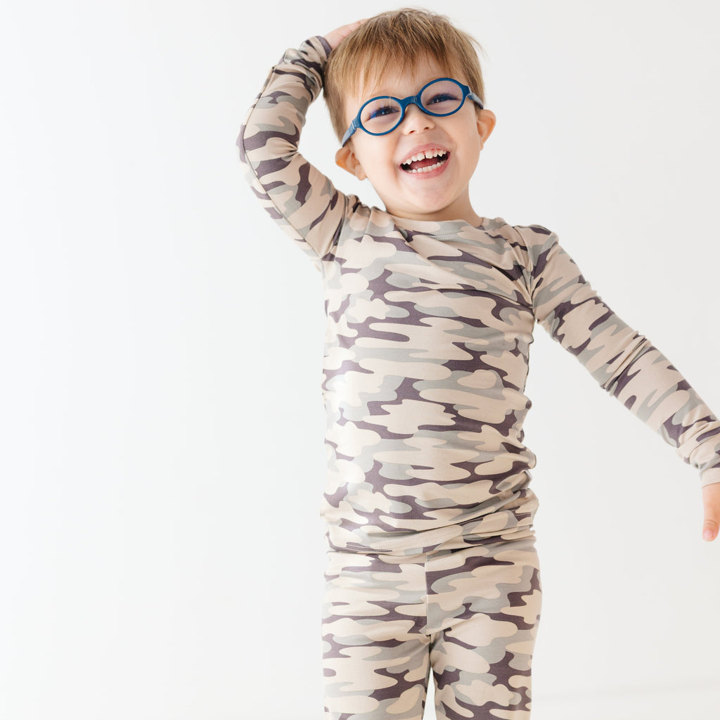 Child wearing a camouflage long sleeve pajama set on a white background